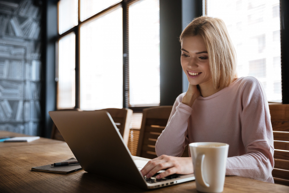 A smiling woman looking at a laptop in a cafe.