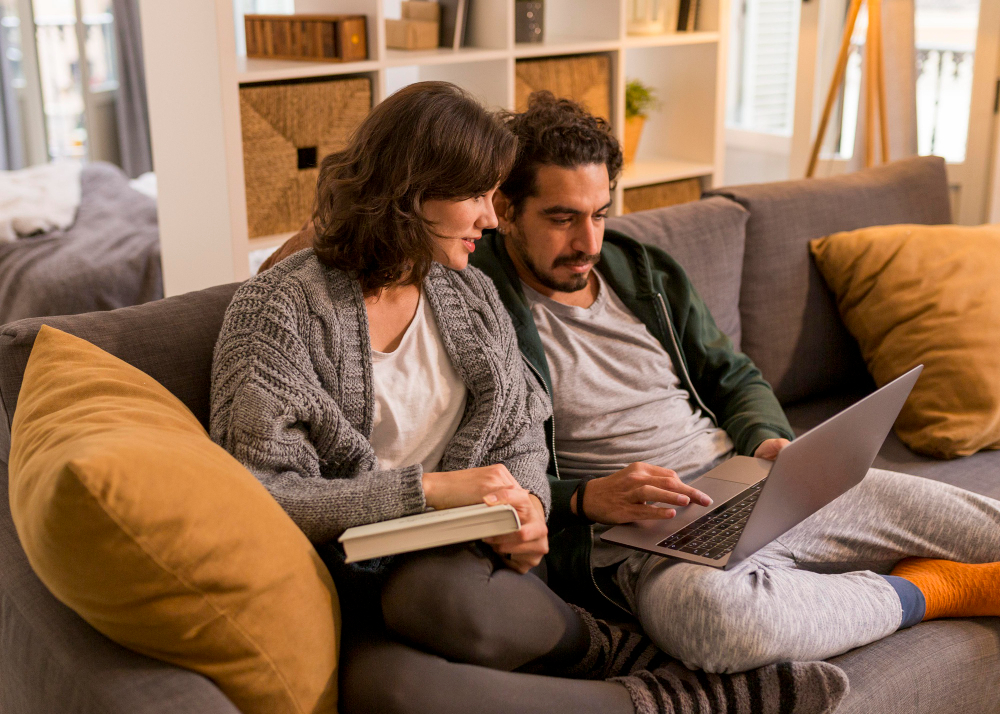 A man and a woman sitting on a sofa while looking at paper and a laptop.