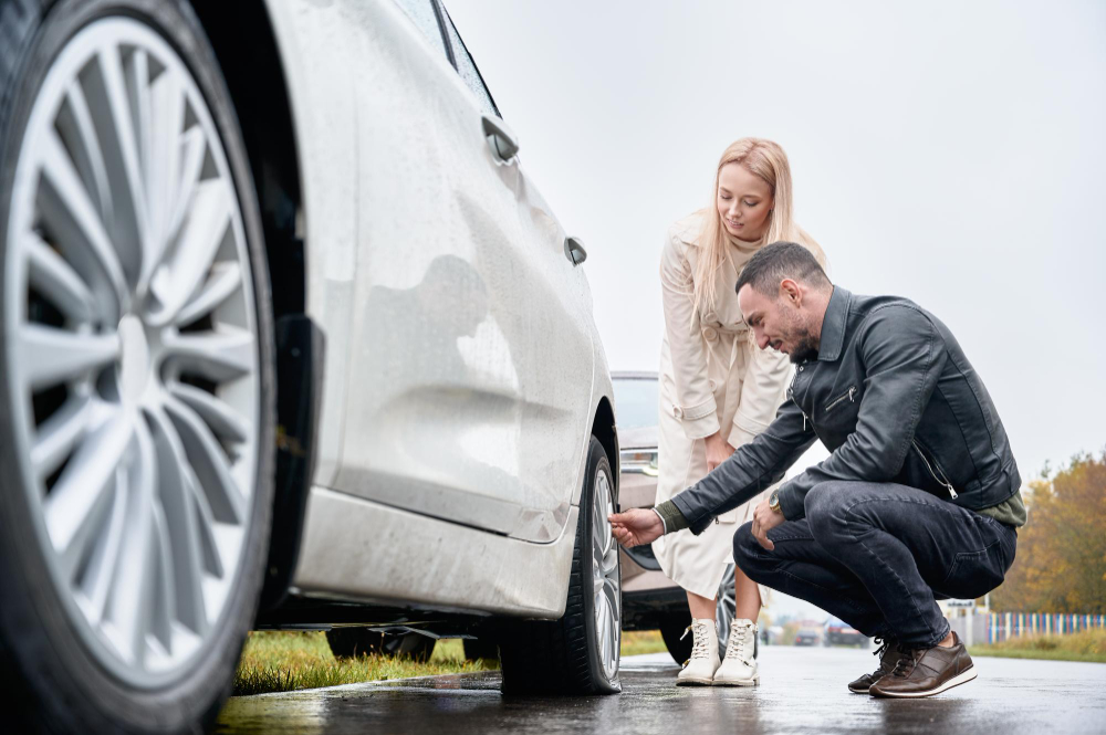 A man and a woman crouch next to the wheel of a car.