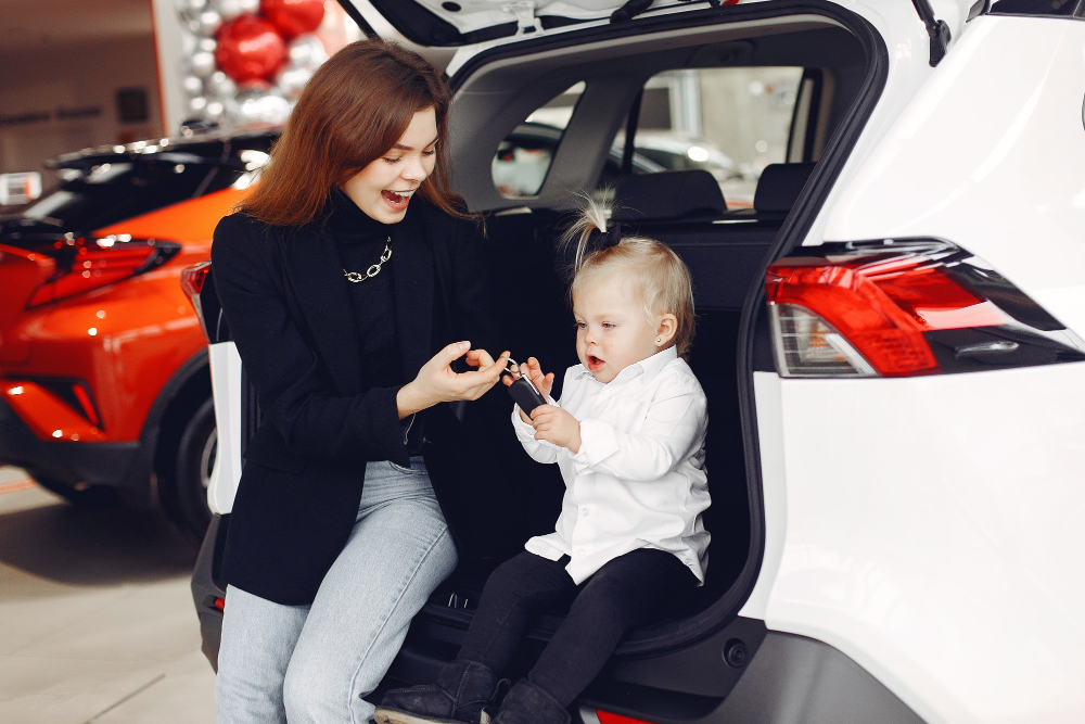An image of a smiling woman with her daughter looking at a new car.
