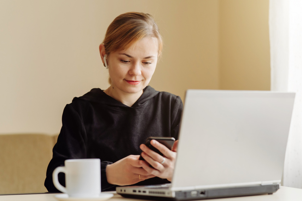 A person looking at a mobile phone and a laptop.